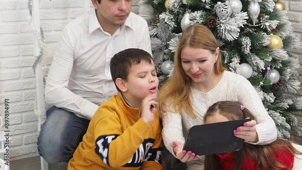 happy family, mom dad son dother Christmas and New Year near the tree with gifts, look at the tablet, communicate online lockdown, virus, covid 19, coronavirus, holidays season 2020 2021. video call. happy family, mom dad son dother Christmas and New Year near the tree with gifts, look at the tablet, communicate online lockdown, virus, covid 19, coronavirus, holidays season 2020 2021. video call.