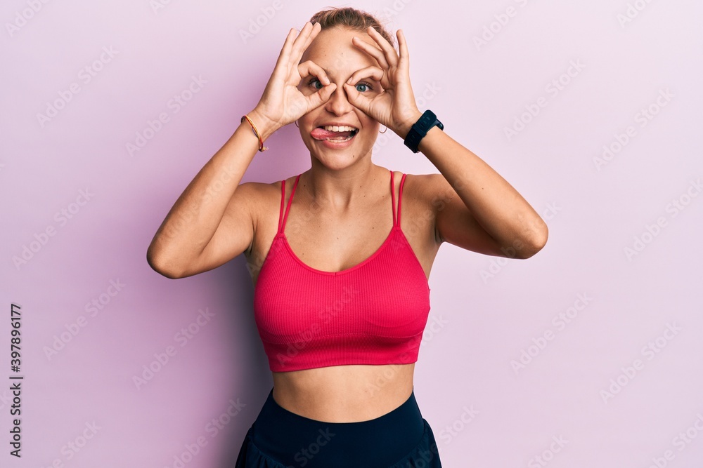 Beautiful caucasian woman wearing sportswear doing ok gesture like binoculars sticking tongue out, eyes looking through fingers. crazy expression. Beautiful caucasian woman wearing sportswear doing ok gesture like binoculars sticking tongue out, eyes looking through fingers. crazy expression.
