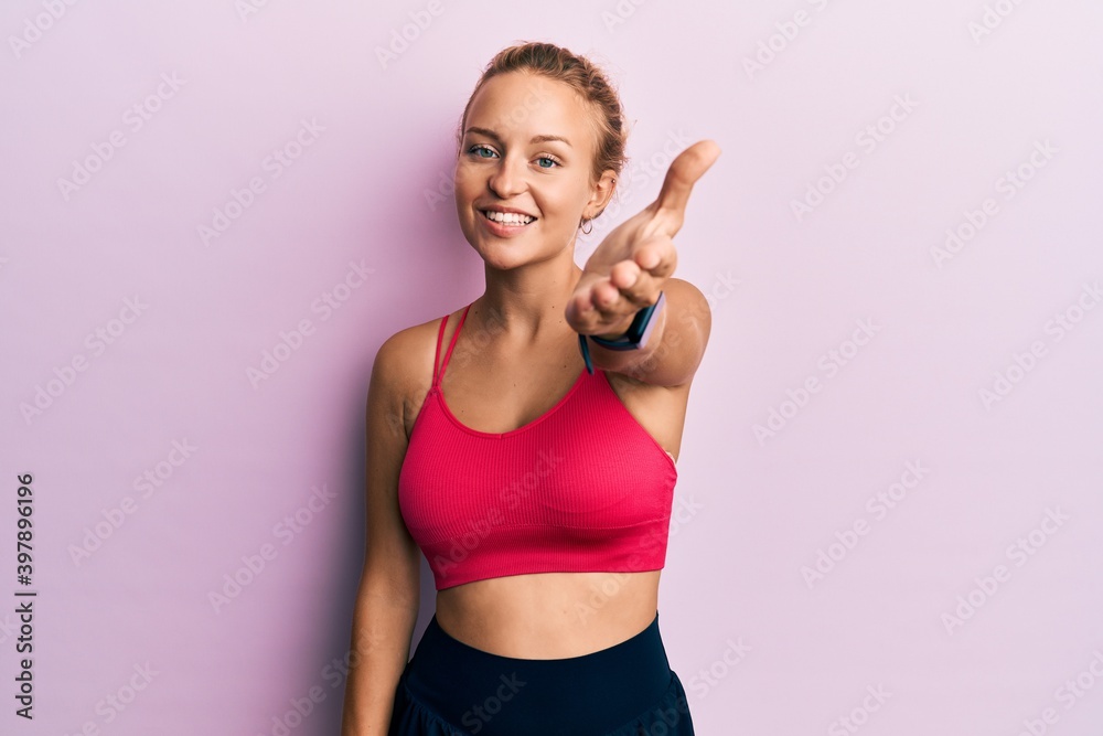 Beautiful caucasian woman wearing sportswear smiling friendly offering handshake as greeting and welcoming. successful business.