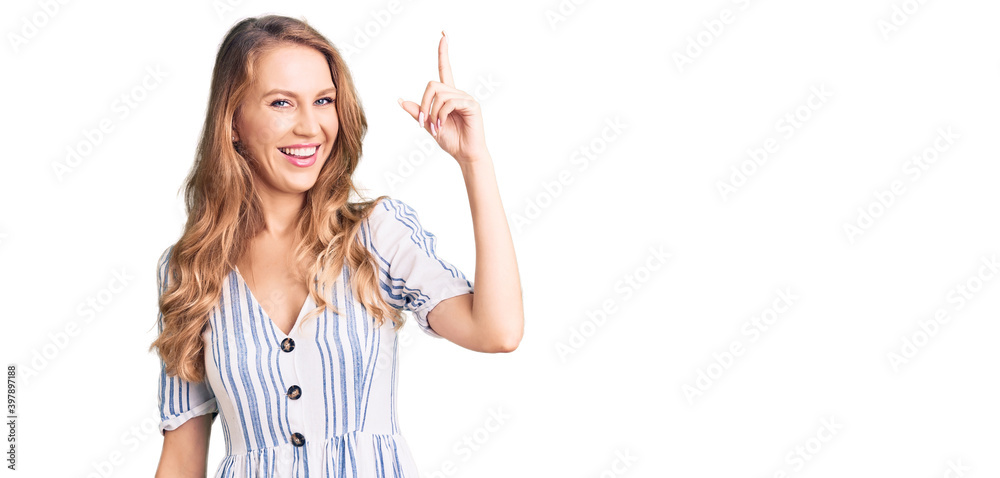Young caucasian woman with blond hair wearing summer dress pointing finger up with successful idea. exited and happy. number one. Young caucasian woman with blond hair wearing summer dress pointing finger up with successful idea. exited and happy. number one.