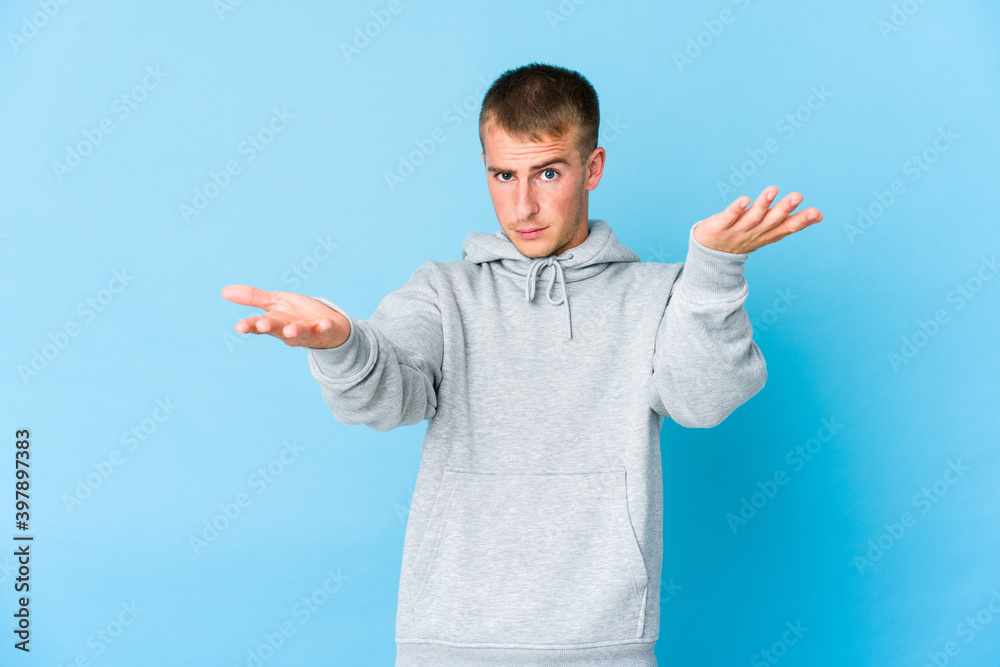Young caucasian handsome man makes scale with arms, feels happy and confident.