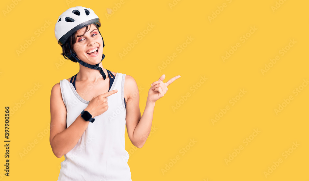 Beautiful young woman with short hair wearing bike helmet smiling and looking at the camera pointing with two hands and fingers to the side. Beautiful young woman with short hair wearing bike helmet smiling and looking at the camera pointing with two hands and fingers to the side.