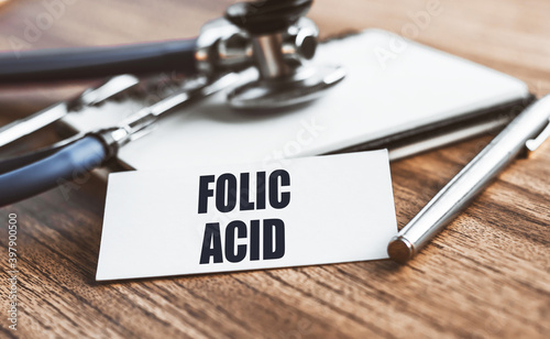 FOLIC ACID text written on card on wooden table with medical background.