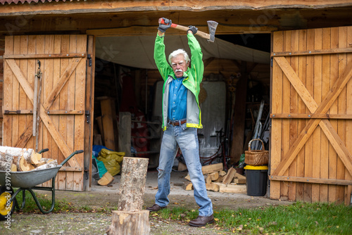 Retired senior man holding the heavy axe. Axe in lumberjack hands chopping or cutting wood trunks.