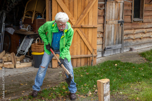 Retired senior man holding the heavy axe. Axe in lumberjack hands chopping or cutting wood trunks.