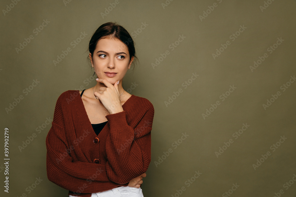 Obraz premium Young short-haired brunette woman. Thinking looking at the left side copy space, supporting her chin with her hand.