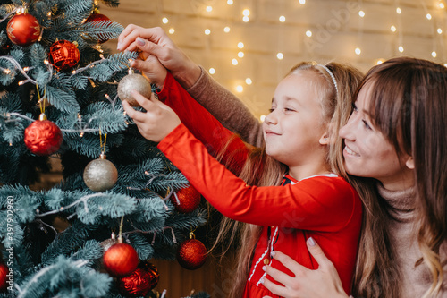 Mother and daughter decorate the Christmas tree together. Traditional parenting.