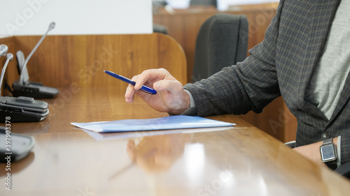 A man in a plaid jacket sits at a table in a large conference room or auditorium in front of a speakerphone. Meeting of professionals. Entrepreneur, lawyer, insurer or teacher