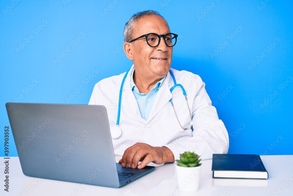 Senior handsome man with gray hair wearing doctor uniform working using computer laptop smiling looking to the side and staring away thinking. Senior handsome man with gray hair wearing doctor uniform working using computer laptop smiling looking to the side and staring away thinking.