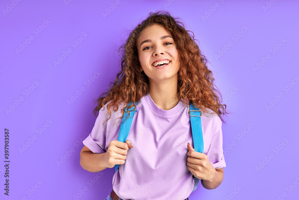 cheerful school girl with bag posing at camera isolated over purple background, cheerful female with curly hair smile, happy to go school. education concept cheerful school girl with bag posing at camera isolated over purple background, cheerful female with curly hair smile, happy to go school. education concept