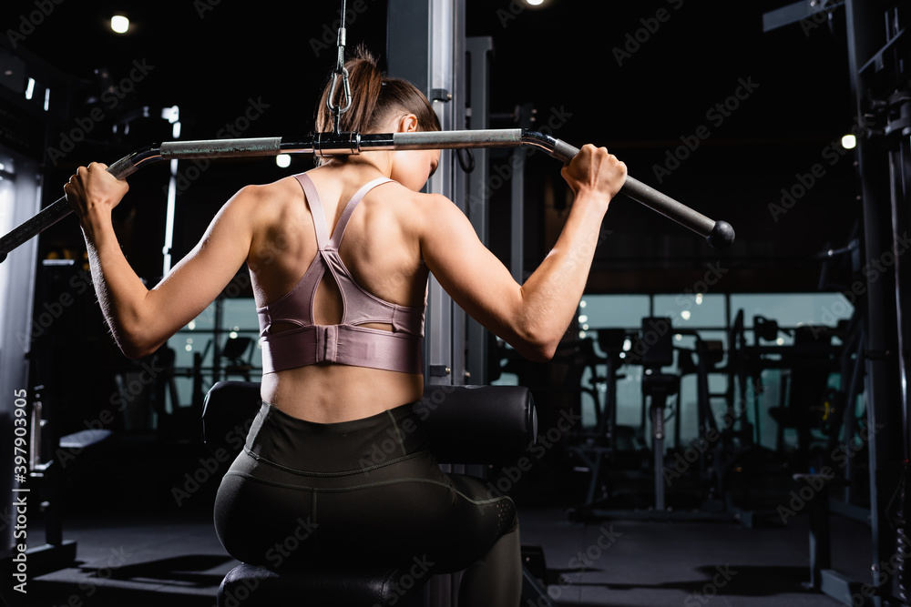 back view of athletic sportswoman doing back and arms extension exercise on lat machine back view of athletic sportswoman doing back and arms extension exercise on lat machine