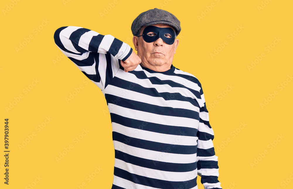 Senior handsome man wearing burglar mask and t-shirt strong person showing arm muscle, confident and proud of power Senior handsome man wearing burglar mask and t-shirt strong person showing arm muscle, confident and proud of power