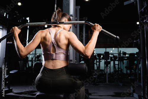 back view of athletic sportswoman doing back and arms extension exercise on lat machine