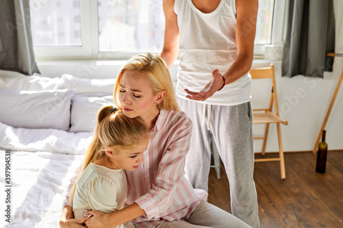 kid girl is suffering from quarrels between parents in the family at home, woman and man argue in the presence of daughter