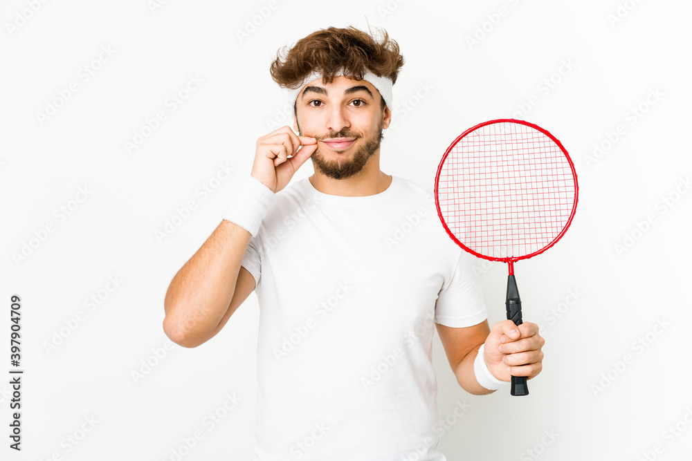 Young indian man playing badminton with fingers on lips keeping a secret.