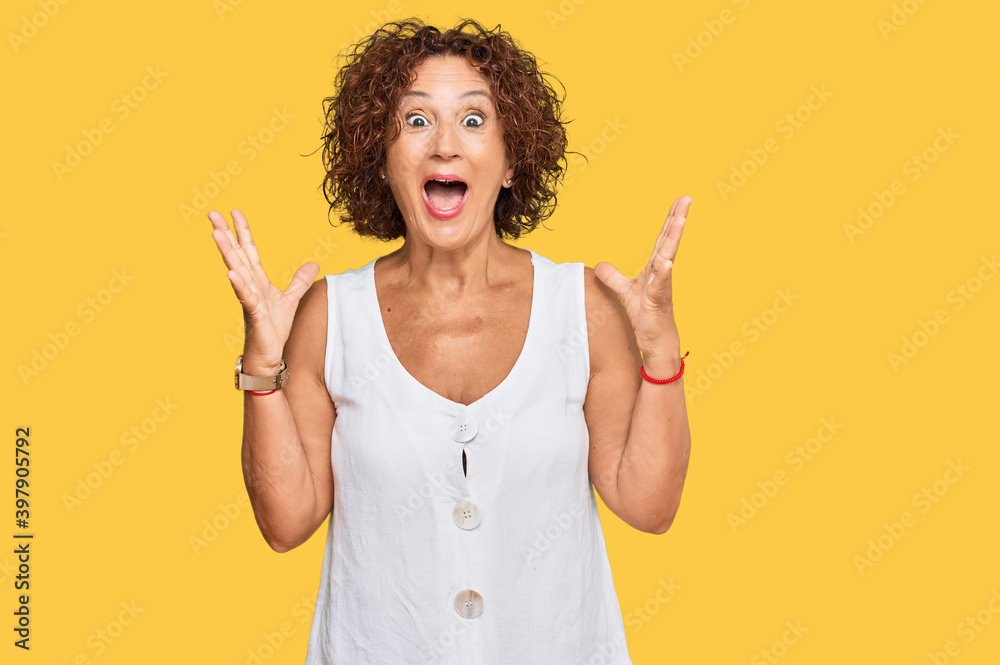 Beautiful middle age mature woman wearing casual white shirt celebrating crazy and amazed for success with arms raised and open eyes screaming excited. winner concept Beautiful middle age mature woman wearing casual white shirt celebrating crazy and amazed for success with arms raised and open eyes screaming excited. winner concept