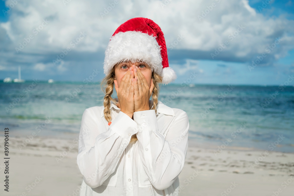 Obraz premium Girl with pigtails and New Year's red hat on the beach. Covers face