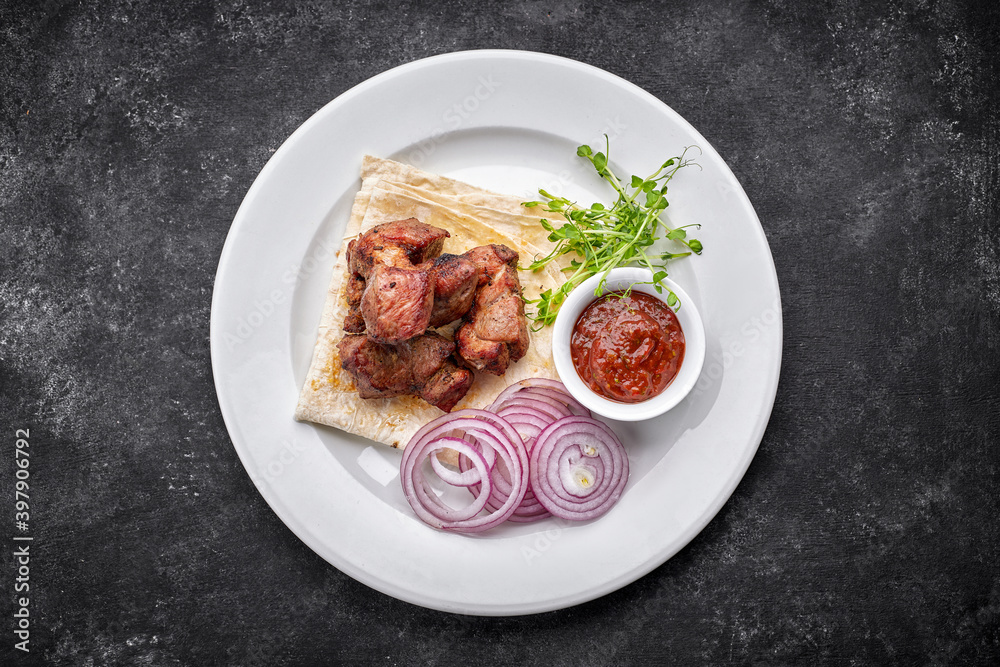 Fried shish kebab with lavash, sauce, microgreen and onion, on a white plate, on a gray background. top view Fried shish kebab with lavash, sauce, microgreen and onion, on a white plate, on a gray background. top view