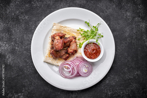 Fried shish kebab with lavash, sauce, microgreen and onion, on a white plate, on a gray background. top view
