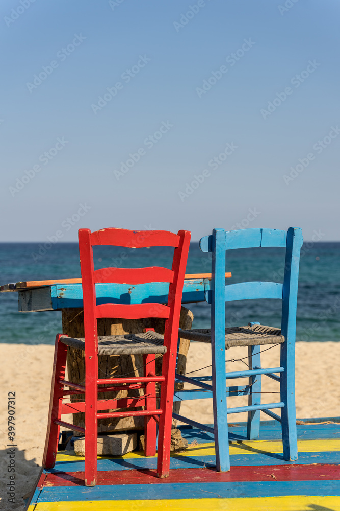 Vivid bright colrful wooden chairs - red and blue standing on the beach of blues sea in the background in Sarti , Greece. 