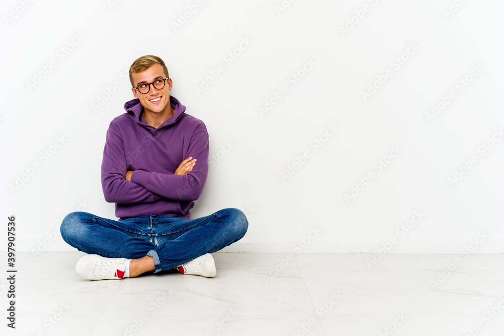 Young caucasian man sitting on the floor smiling confident with crossed arms.
