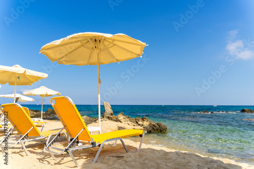 Rows of yellow beach umbrellas and sun beds on the white sand close to the crystal clear waster of Mediterranean sea. Ideal 5 star blue flag beach in Greece  Halkidiki. Tourist paradise. 