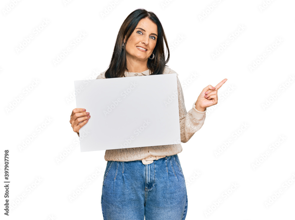 Middle age brunette woman holding blank empty banner smiling happy pointing with hand and finger to the side Middle age brunette woman holding blank empty banner smiling happy pointing with hand and finger to the side