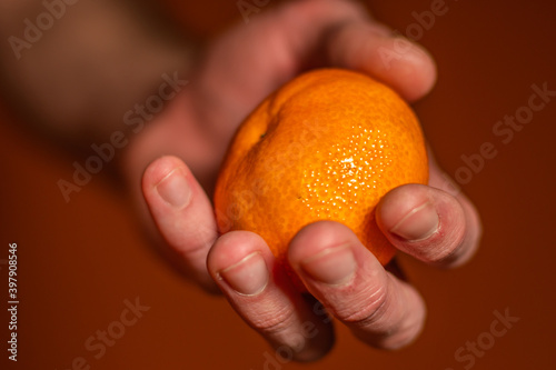 Man's hand holds a tangerine on an orange background, close-up.