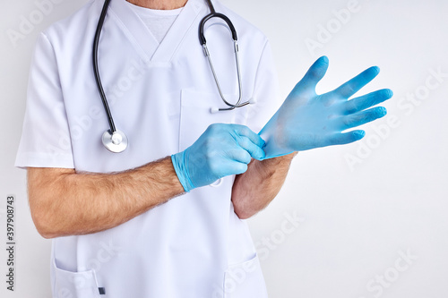 cropped male doctor is wearing gloves preparing for work, wearing white robe, isolated in studio with white background