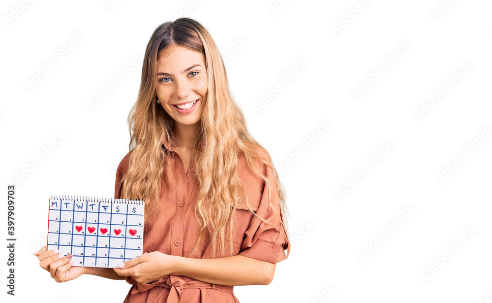Beautiful caucasian woman with blonde hair holding heart calendar looking positive and happy standing and smiling with a confident smile showing teeth Beautiful caucasian woman with blonde hair holding heart calendar looking positive and happy standing and smiling with a confident smile showing teeth