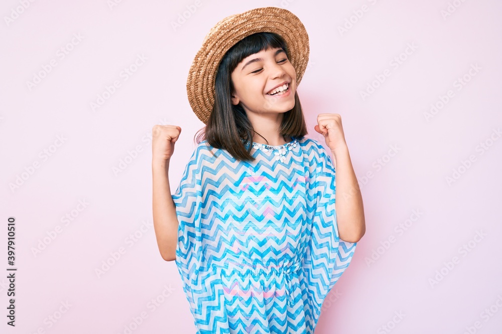 Young little girl with bang wearing summer dress and hat very happy and excited doing winner gesture with arms raised, smiling and screaming for success. celebration concept. Young little girl with bang wearing summer dress and hat very happy and excited doing winner gesture with arms raised, smiling and screaming for success. celebration concept.