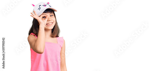 Young little girl with bang wearing funny kitty cap smiling happy doing ok sign with hand on eye looking through fingers