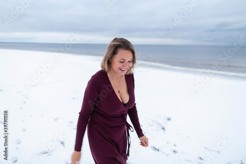 Curvy girl in the burgundy dress on the background of the winter sea. Portrait of a woman having fun on sea coast , windy weather, cold atmospheric image.