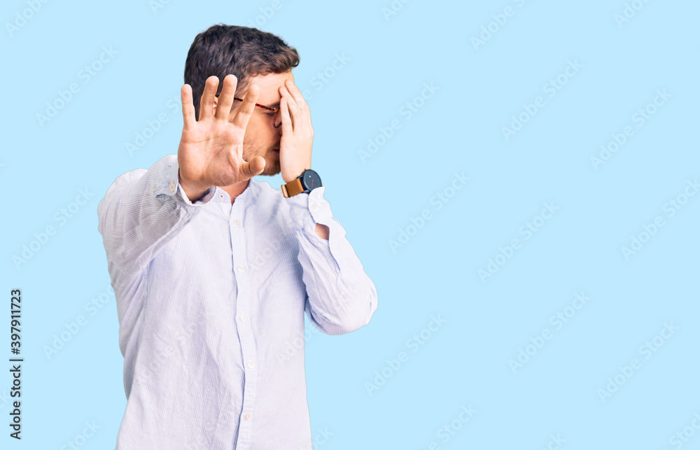 Handsome young man with bear wearing elegant business shirt and glasses covering eyes with hands and doing stop gesture with sad and fear expression. embarrassed and negative concept. Handsome young man with bear wearing elegant business shirt and glasses covering eyes with hands and doing stop gesture with sad and fear expression. embarrassed and negative concept.