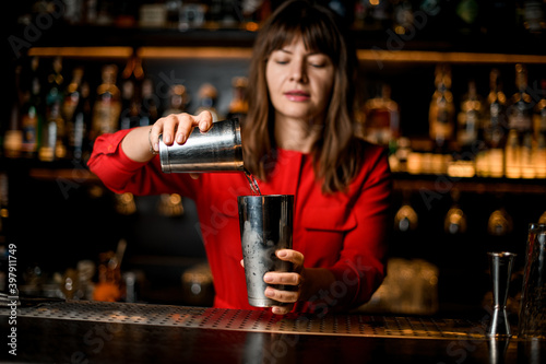 close-up of female bartender hands holding shaker glasses and pouring liquid