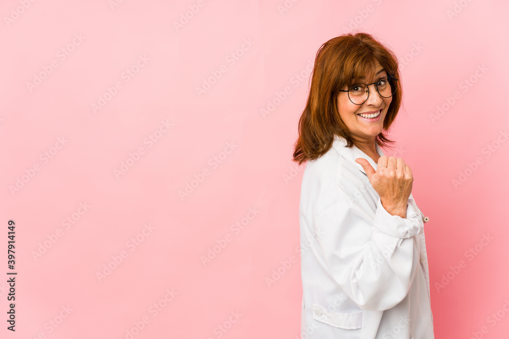Middle age caucasian doctor woman isolated points with thumb finger away, laughing and carefree. Middle age caucasian doctor woman isolated points with thumb finger away, laughing and carefree.