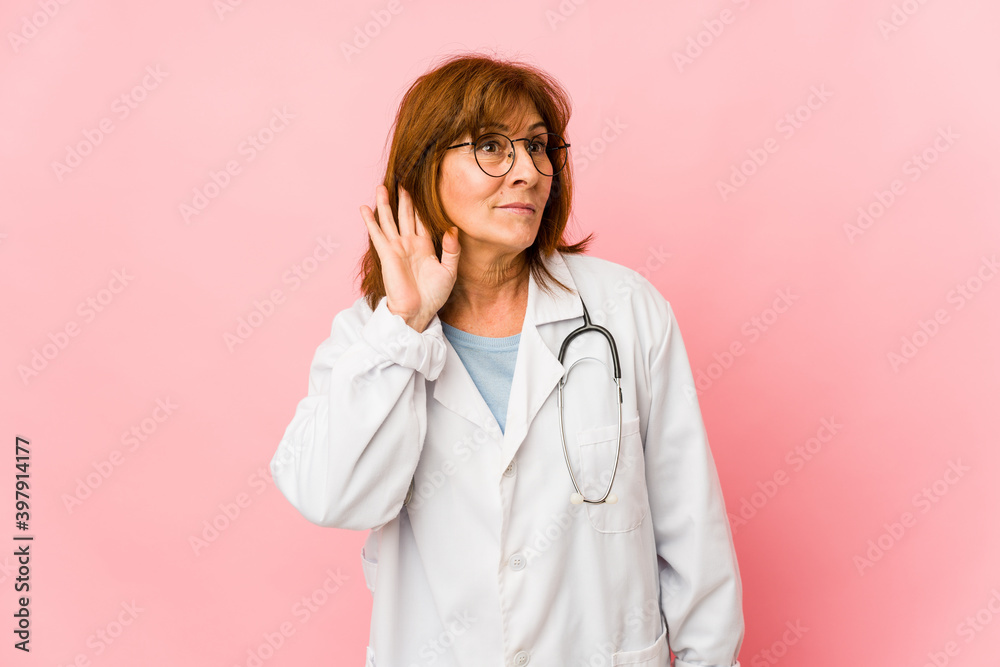 Middle age caucasian doctor woman isolated trying to listening a gossip.