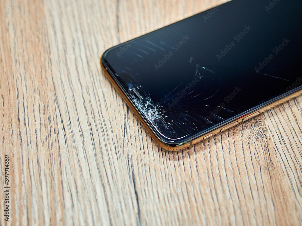 Photo of gold smartphone with broken damaged display. Modern smartphone with damaged glass screen on wood background. Device needs repair. Photo of gold smartphone with broken damaged display. Modern smartphone with damaged glass screen on wood background. Device needs repair.