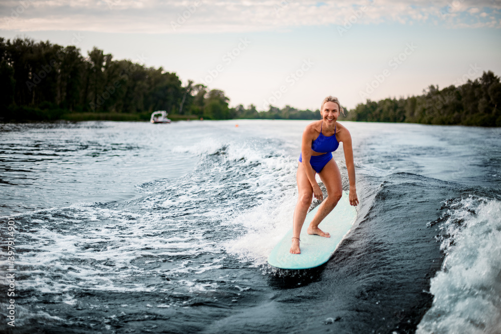 smiling woman balances on surfboard while riding the wave.