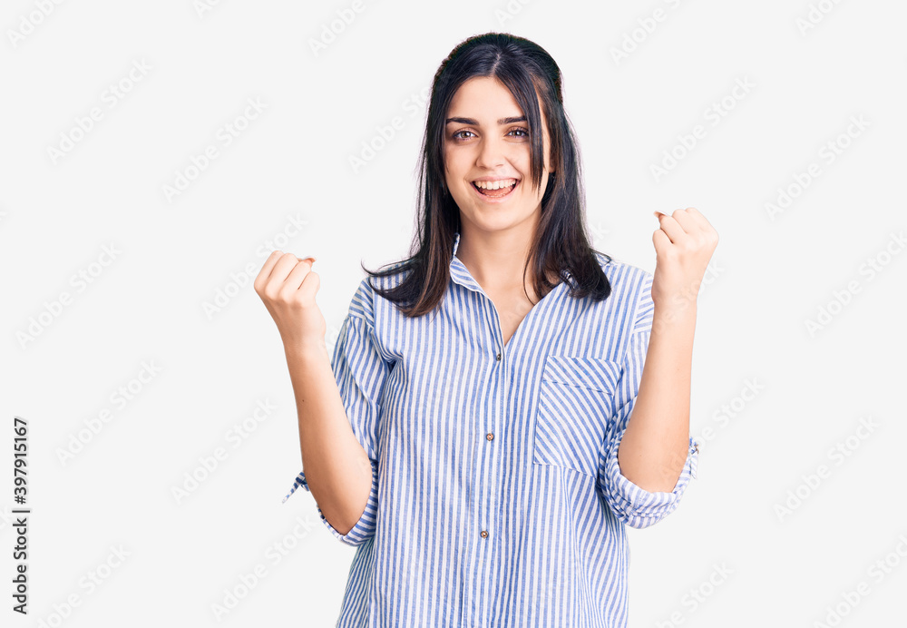 Young beautiful girl wearing striped shirt screaming proud, celebrating victory and success very excited with raised arms Young beautiful girl wearing striped shirt screaming proud, celebrating victory and success very excited with raised arms