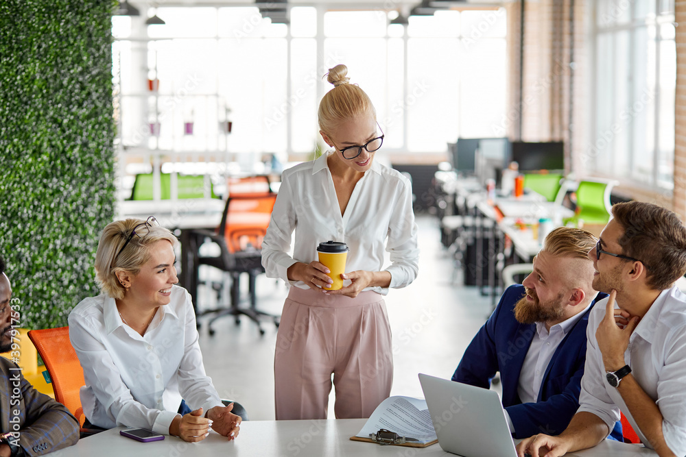 Fototapeta premium female company director have nice talk with employees, discuss projects on headline, take a break, woman stand with cup of coffee and smile, in the office