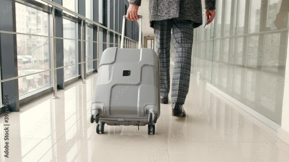Handsome mature businessman in the costume going by the corridor of the airport with a suitcase . Handsome mature businessman in the costume going by the corridor of the airport with a suitcase .