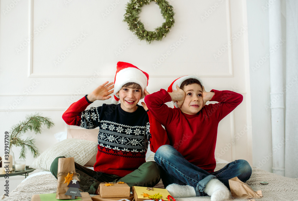 Fototapeta premium Cute boys brothers pack Christmas gifts sitting on the bed at home. new year surprise