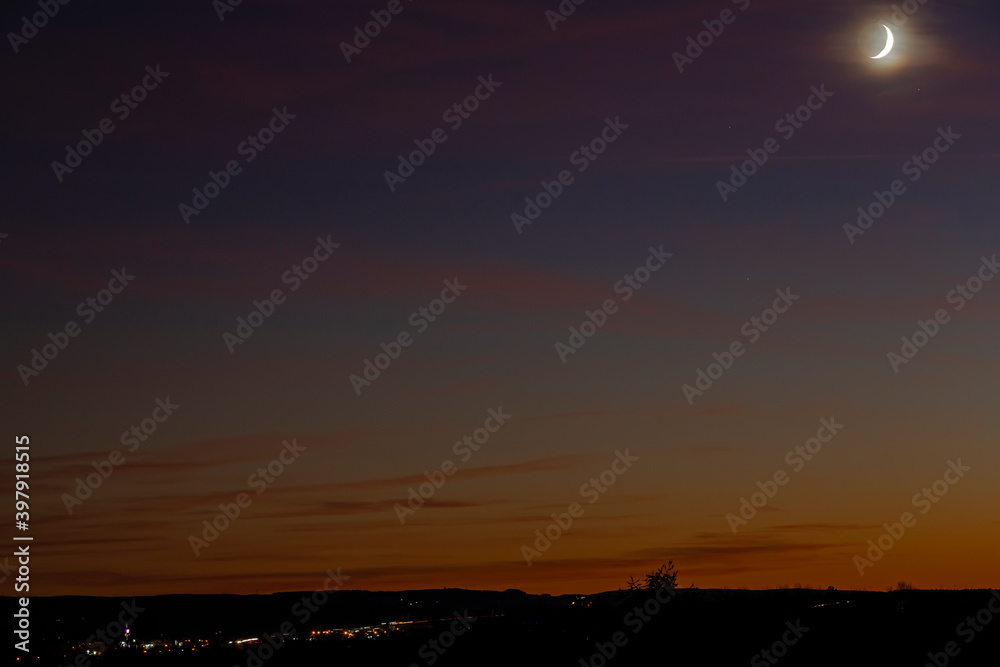 Waxing crescent moon in a beautiful dusk landscape during autumn season.