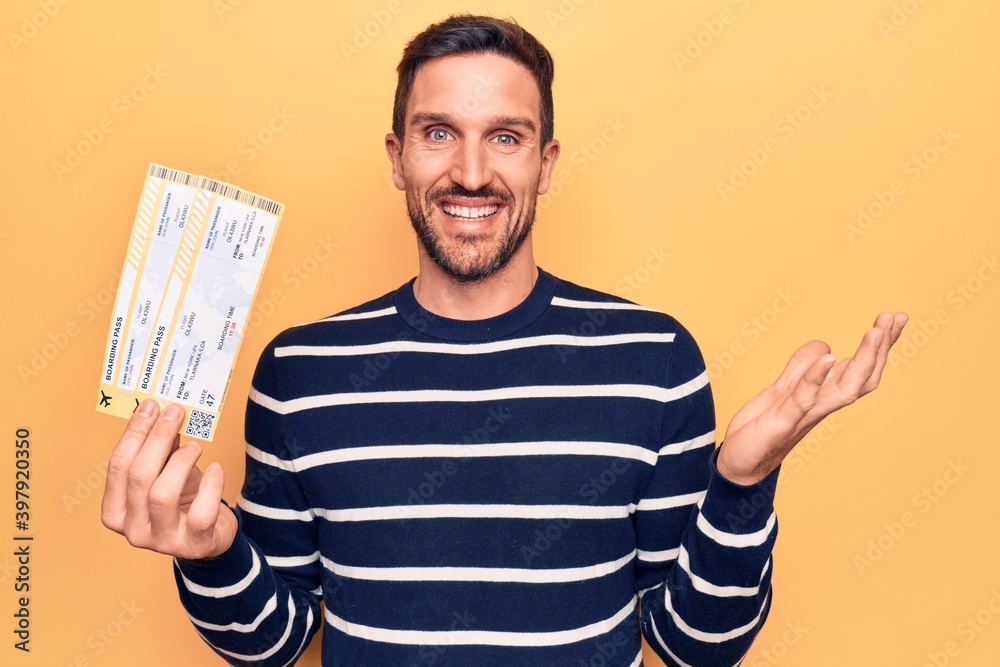 Young handsome tourist man on vacation holding airline boarding pass over yellow background celebrating achievement with happy smile and winner expression with raised hand Young handsome tourist man on vacation holding airline boarding pass over yellow background celebrating achievement with happy smile and winner expression with raised hand