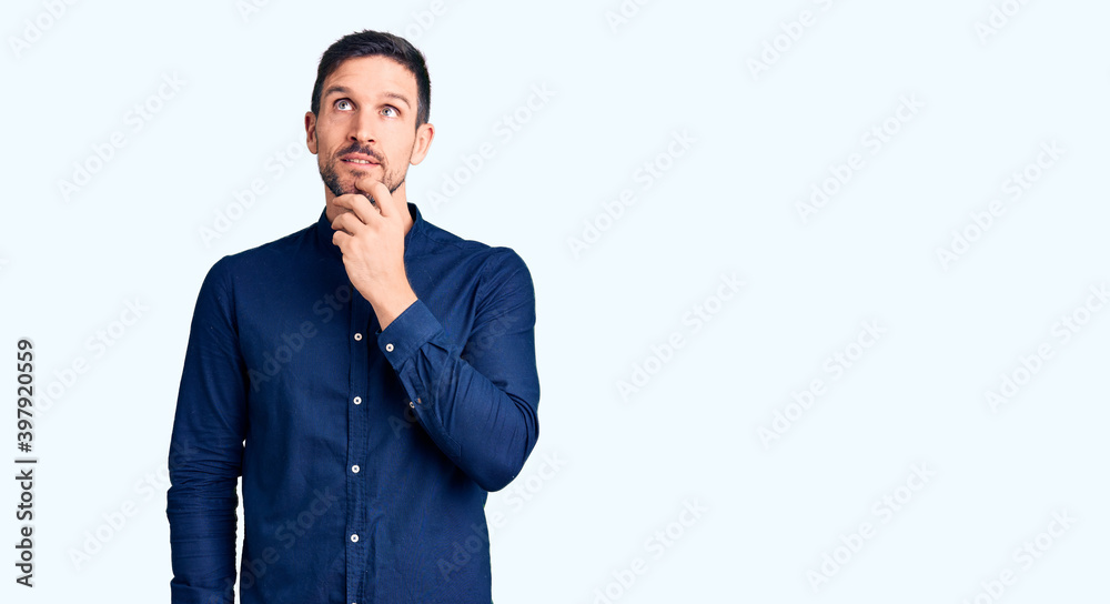 Young handsome man wearing casual shirt with hand on chin thinking about question, pensive expression. smiling and thoughtful face. doubt concept. Young handsome man wearing casual shirt with hand on chin thinking about question, pensive expression. smiling and thoughtful face. doubt concept.