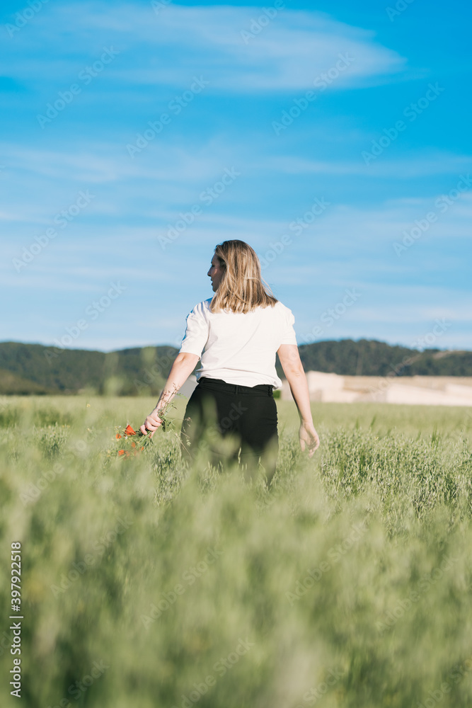 Outdoor portrait of a beautiful woman with poppy flowers in a wheat field.
