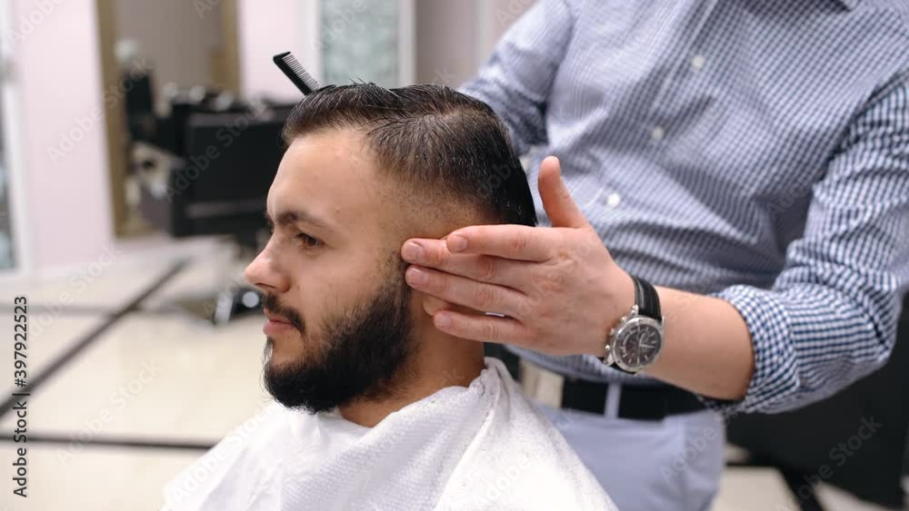 professional male hairdresser cuts the hair of a young positive man with scissors, looks at the camera and smiles. Happy client gets a haircut at the barber. professional male hairdresser cuts the hair of a young positive man with scissors, looks at the camera and smiles. Happy client gets a haircut at the barber.