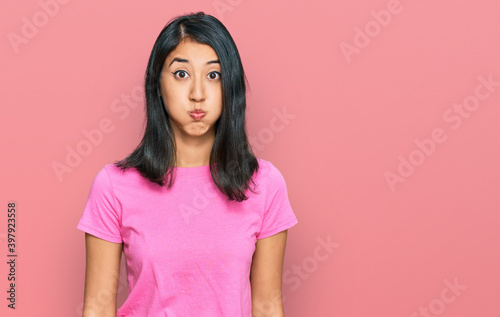 Beautiful asian young woman wearing casual pink t shirt puffing cheeks with funny face. mouth inflated with air, crazy expression.