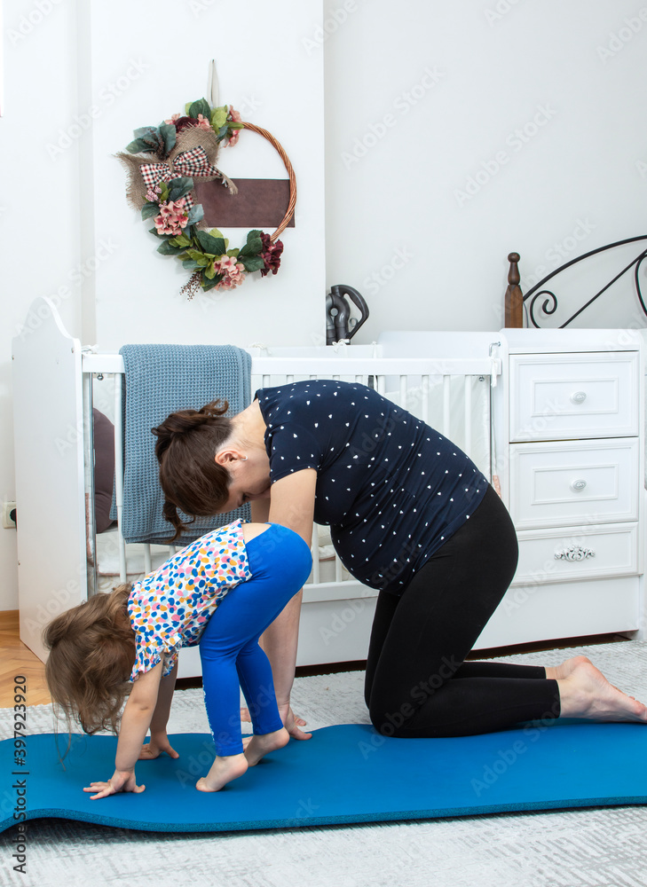 Portrait of adorable cute little girl with young pregnant mother doing yoga  exercise together. Mothers day. Happy family. Maternity during coronavirus  pandemic and quarantine. Stock Photo
